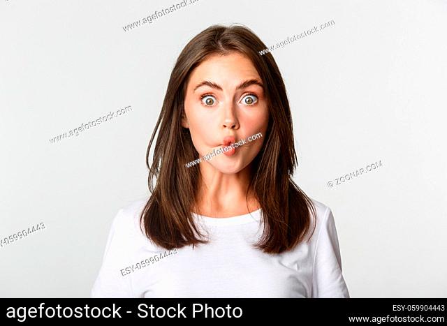Close-up of funny and cute brunette girl suckink lips, making fish grimace, white background