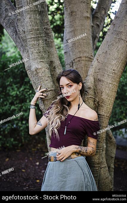 Portrait of young woman leaning on tree in park
