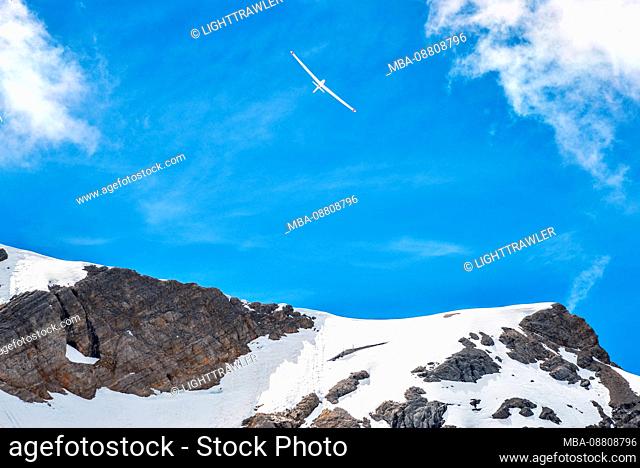 Snow-covered summit with glider in front of summery sky