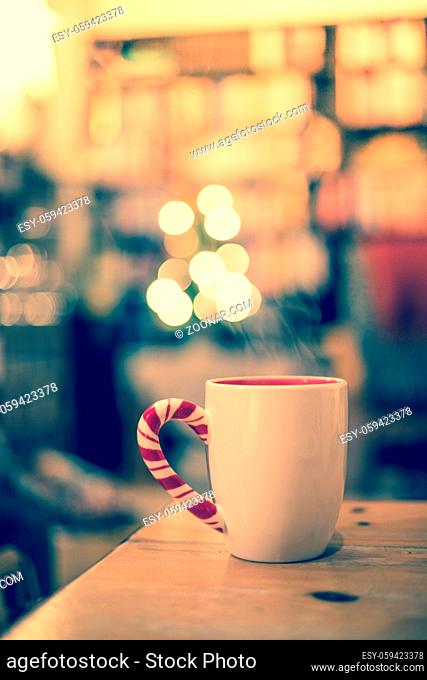 White cup of tea is standing on a wooden table. Steam and blurry background whit lights