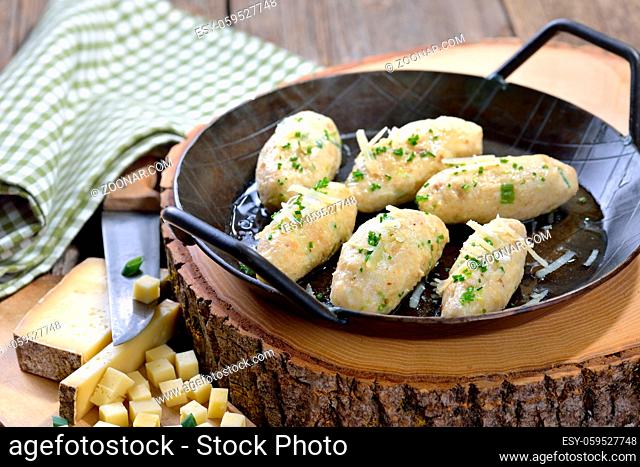 Deftige Südtiroler Kasnocken mit gebräunter Butter und Parmesen rustikal in der Pfanne serviert - South Tyrolean cheese dumplings made of white bread and...