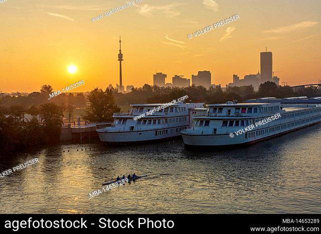 Vienna, rowing boat at sunrise at river Donau (Danube), school ship of Bertha-von-Suttner-Gymnasium, view to Donauturm and Donaucity with DC Tower 1 in 22