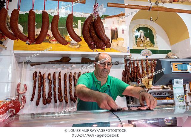 Owner and butcher places out tasting pieces of homemade spanish sausages - calle Juan Relinque, Vejer de la Frontera, Andalusia, Spain