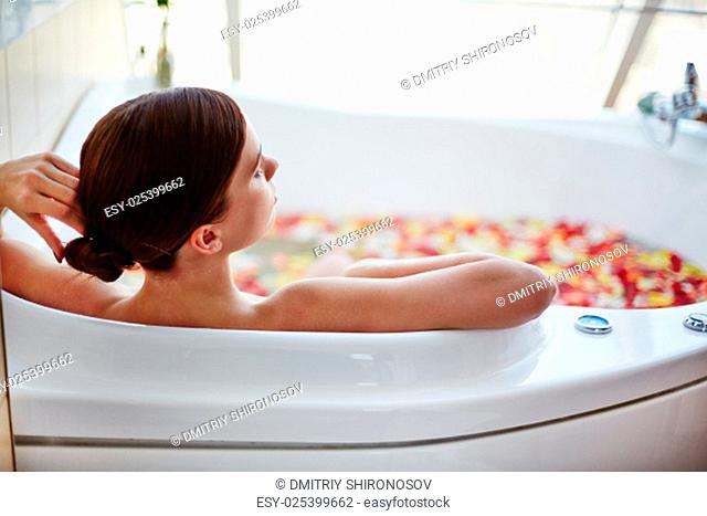 Relaxed woman sitting in bath with rose petals