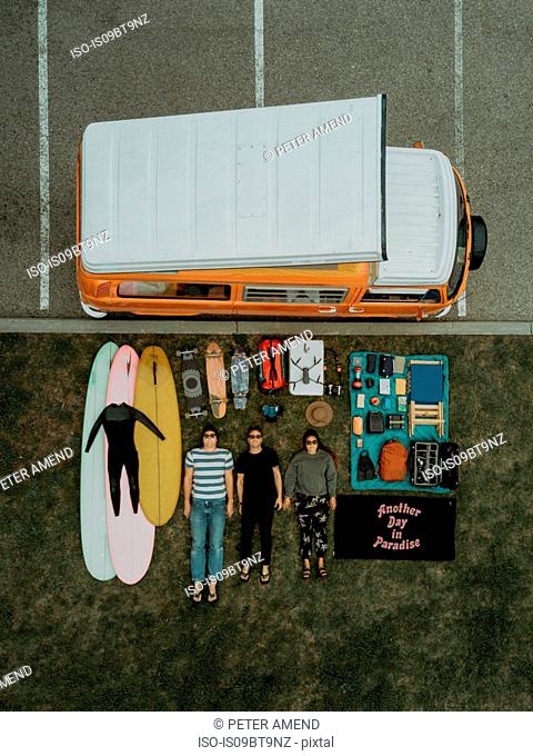 Three young surfers with surfing equipment and recreational vehicle lying on backs by beach carpark, overhead portrait, Ventura, California, USA