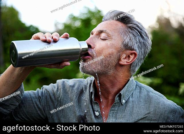 Thirsty man spilling while drinking water from bottle in forest
