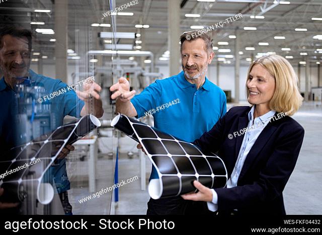 Mature male and female professionals discussing by glass in factory