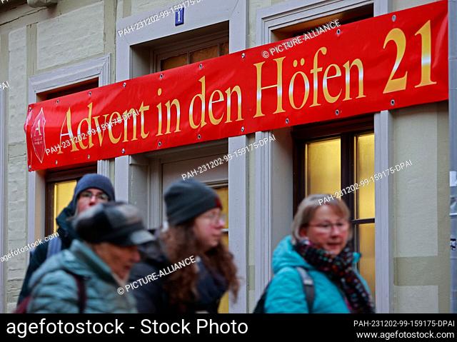 02 December 2023, Saxony-Anhalt, Quedlinburg: Visitors walk past a sign with the inscription ""Advent in den Höfen"". Advent in den Höfen has been around for...
