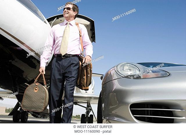 Mid-adult businessman in front of car and airplane