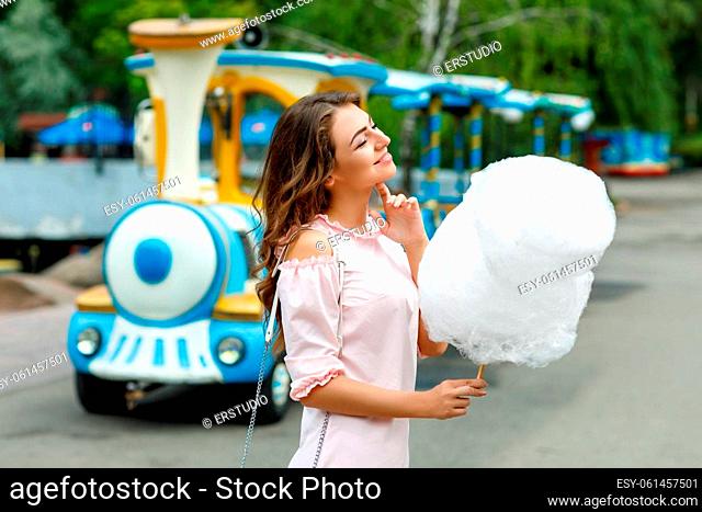 young attractive woman holding sweet cotton candy in an amusement park