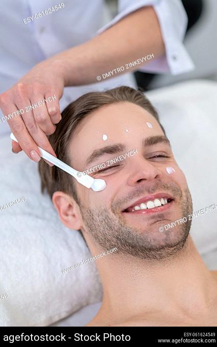 Moisturizing procedure. Cosmetologist applying moisturizing cream on clients face