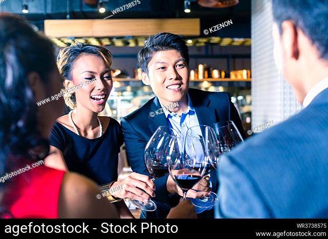 Asian friends toasting with red wine in bar or restaurant