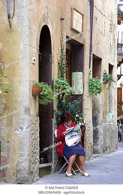 Italy, Tuscany, Pienza, alley, entrance, woman, chair, sits, newspaper reads, , city, idyllically, residence, stone-house, business, facade, windows, entrance