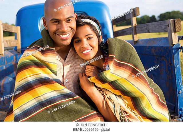 Couple wrapped in blanket sitting on back of truck