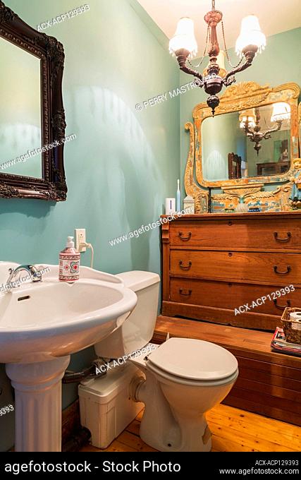 White pedestal sink with electric flush toilet, antique wooden mirror and dresser in bathroom with pinewood plank floorboards on upstairs floor inside an old...
