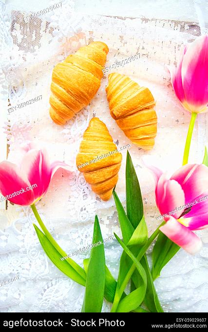 Three croissants and bright pink tulips on lace tablecloth