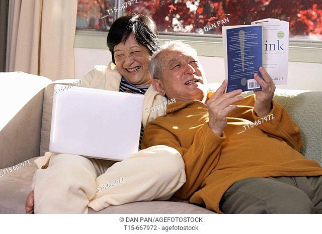 Senior Asian couple having fun spending time together by reading and surfing internet on laptop