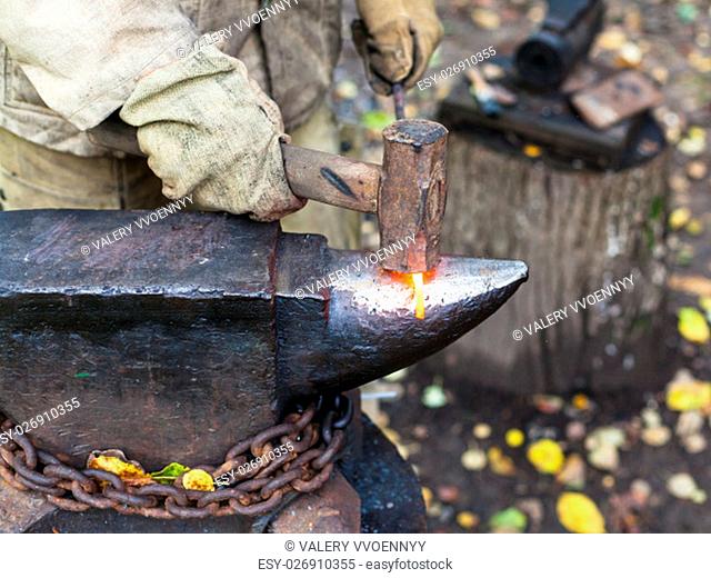 Blacksmith processing red hot iron rod on anvil in outdoor rural smithy