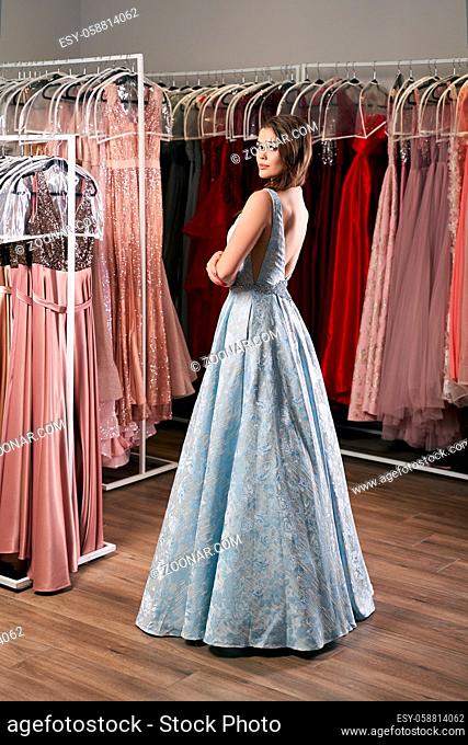 Young beautiful blonde girl wearing a full-length draped sky blue satin slit prom ball gown decorated with embroindered roses pattern
