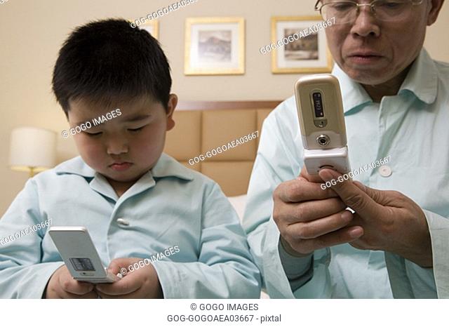 Middle-aged man and grandson using cell phones in pajamas