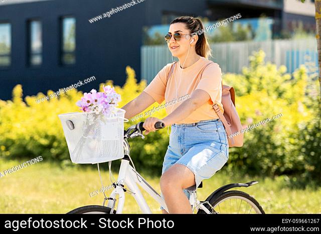 happy woman with earphones riding bicycle in city