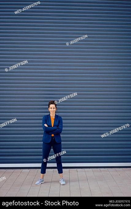 Businesswoman with arms crossed standing in front of closed shutter on footpath