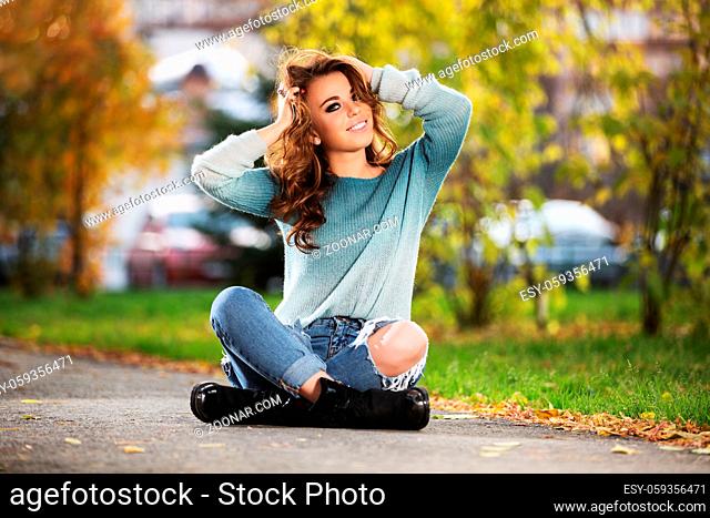 Happy young fashion woman with long curly hairs sitting on city street