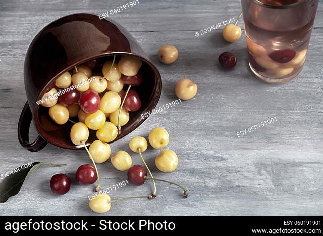 On the table, yellow and red cherries spilled out of a ceramic cup. Front view, copy space