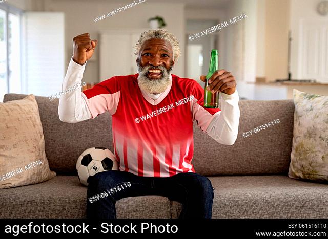 Senior man holding beer bottle cheering while watching sports on TV