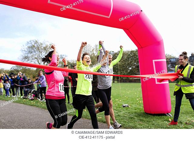 Enthusiastic family runners crossing charity run finish line in park