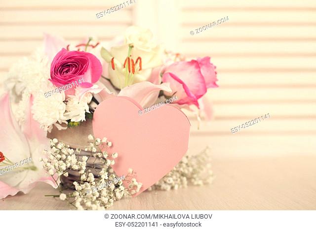 Beautiful bouquet of flowers in basket and heart shaped valentines day card on wooden background