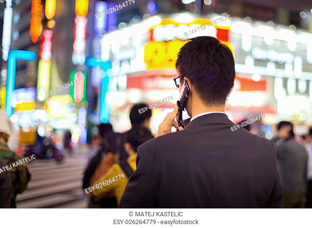 Japanese corporative businessman in suit, after work, talking on cell phone while waiting on crossroad in Kabukicho, entertainment and red-light district in...