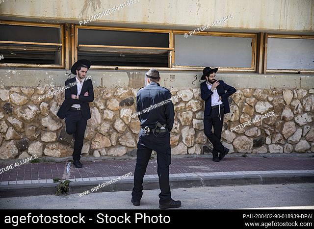 02 April 2020, Israel, Bnei Brak: An Israeli policeman stops Orthodox Jews, who insist on carrying on with their prayer at the Ponevezh Yeshiva