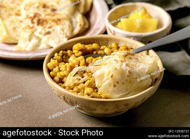 Traditional indian yellow pea dal with roti flatbread and lemons