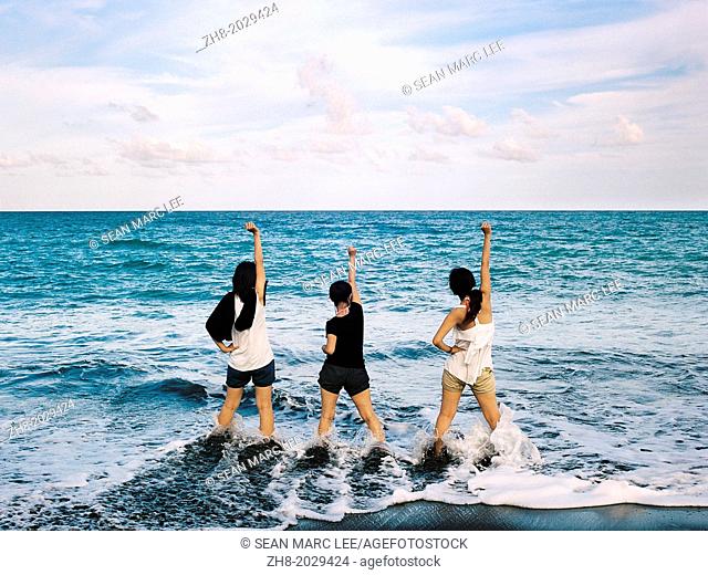 Three young woman hold their fist high out to the open ocean along the coast of Taiwan