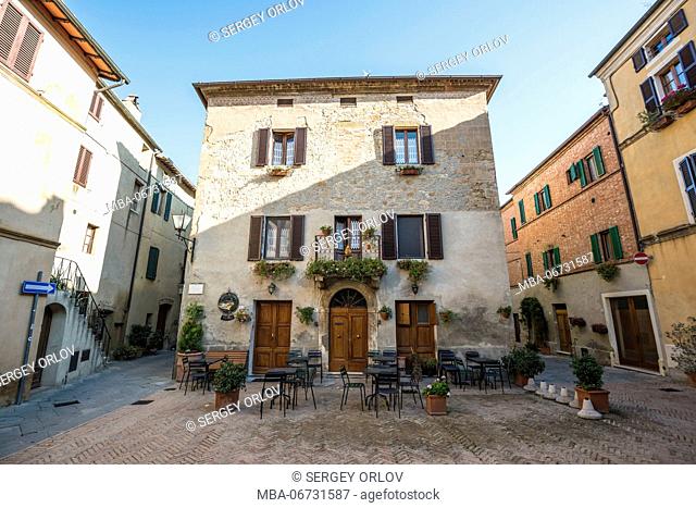 A small stone square of Pienza with café tables, chairs and an attractive house with flower-decorated balcony