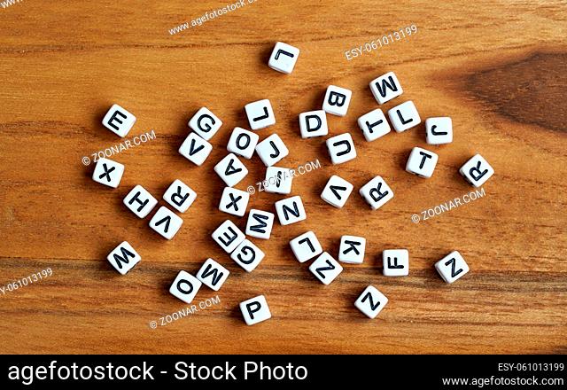 Small white cube beads with various letters scattered on wooden board, view from above