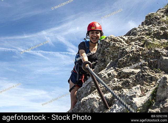 Laughing young woman with climbing helmet and on rock secured with rope, female climber on a via ferrata, Mittenwald via ferrata, Karwendel Mountains