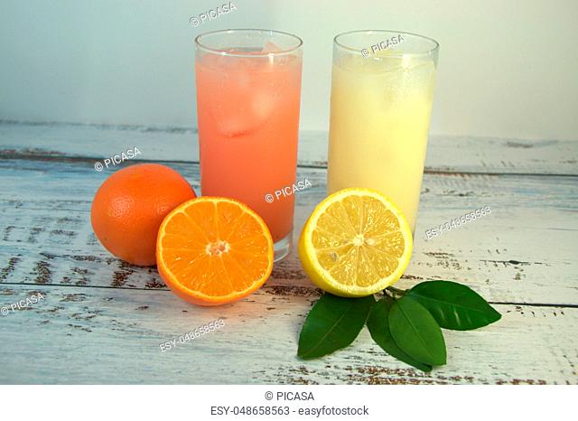 Two glass glasses with a refreshing juice and ice, on a textile stand, whole and sliced half of an orange with leaves and half a lemon