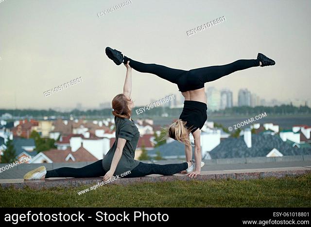 Two young female gymnasts doing acrobatics elements with cityscape on background, horizontal