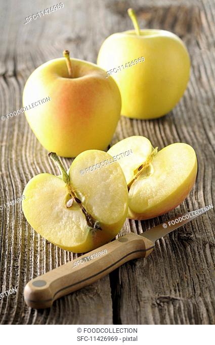 Golden Delicious apples, whole and halved, on a wooden surface