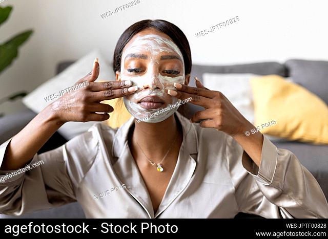 Young woman with fingers applying facial mask