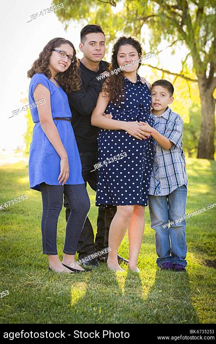 Happy attractive hispanic family with their pregnant mother outdoors at the park
