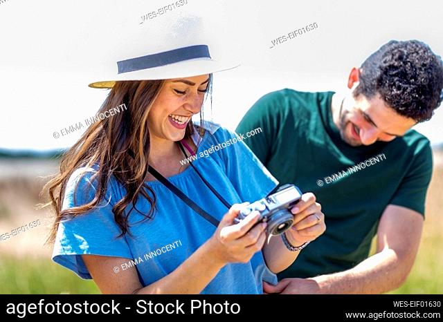 Cheerful girlfriend checking camera by boyfriend on sunny day