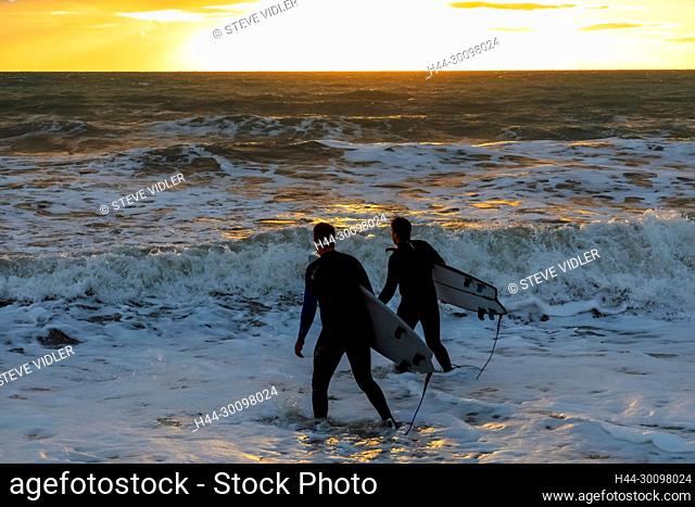 England, East Sussex, Eastbourne, Birling Gap, The Seven Sisters Cliffs and Beach, Two Male Surfers Walking on Beach Carrying Surfboards
