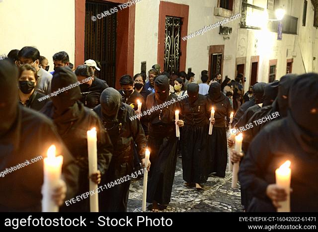 TAXCO, MEXICO - APR 15, 2022: A woman penitent wears a black robe while holding candles, taking part in the procession of silence as part of the Holy Week...
