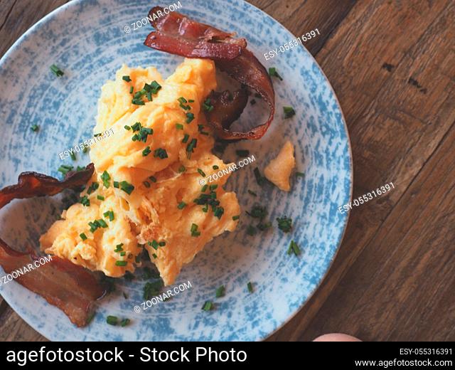 Tasty scrambled eggs with bacon and chives on a rustic wooden table, tsty breakfast concept, view from above