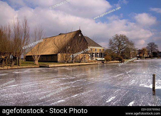 Frozen river the Graafstroom with on the other side a monumental farm in the South Holland village of Bleskensgraaf