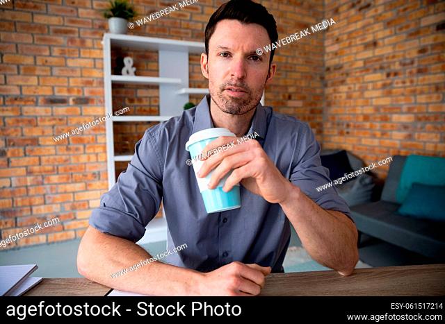 Portrait of man holding coffee cup while sitting on his desk