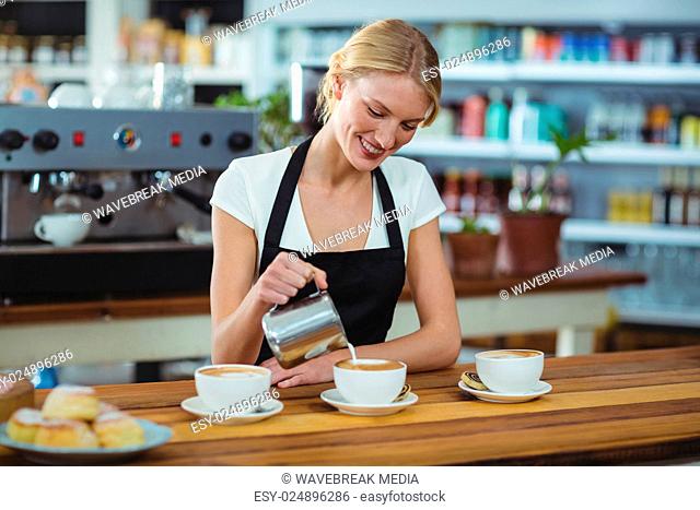 Smiling waitress making cup of coffee at counter